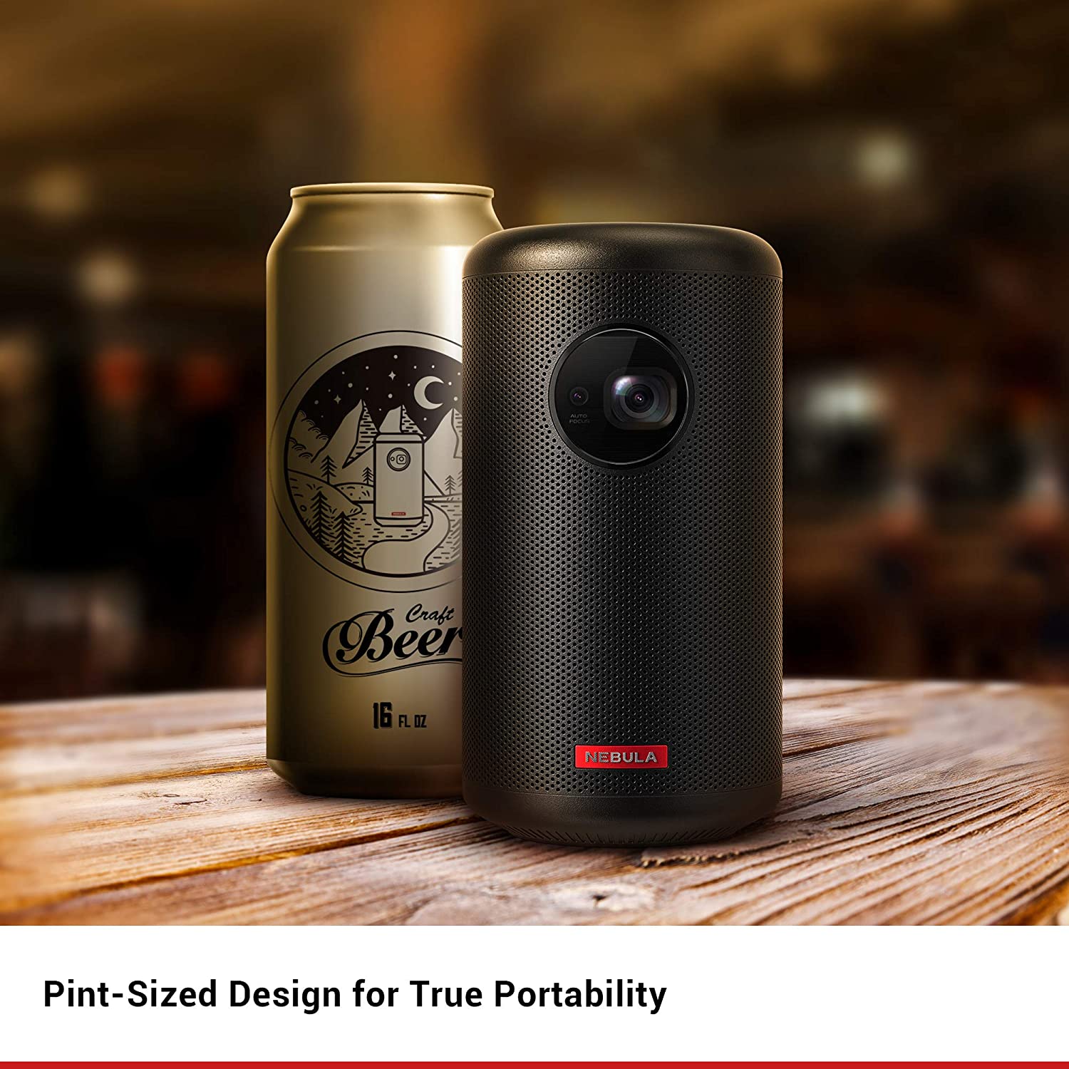 A Nebula Capsule II portable projector sits on a wooden table next to a can of beer.